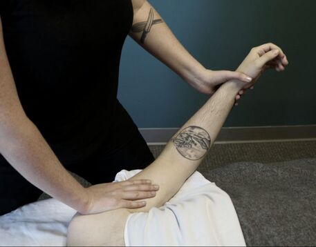 Picture of a massage therapist's torso, with her hands in place stretching out a client's arm